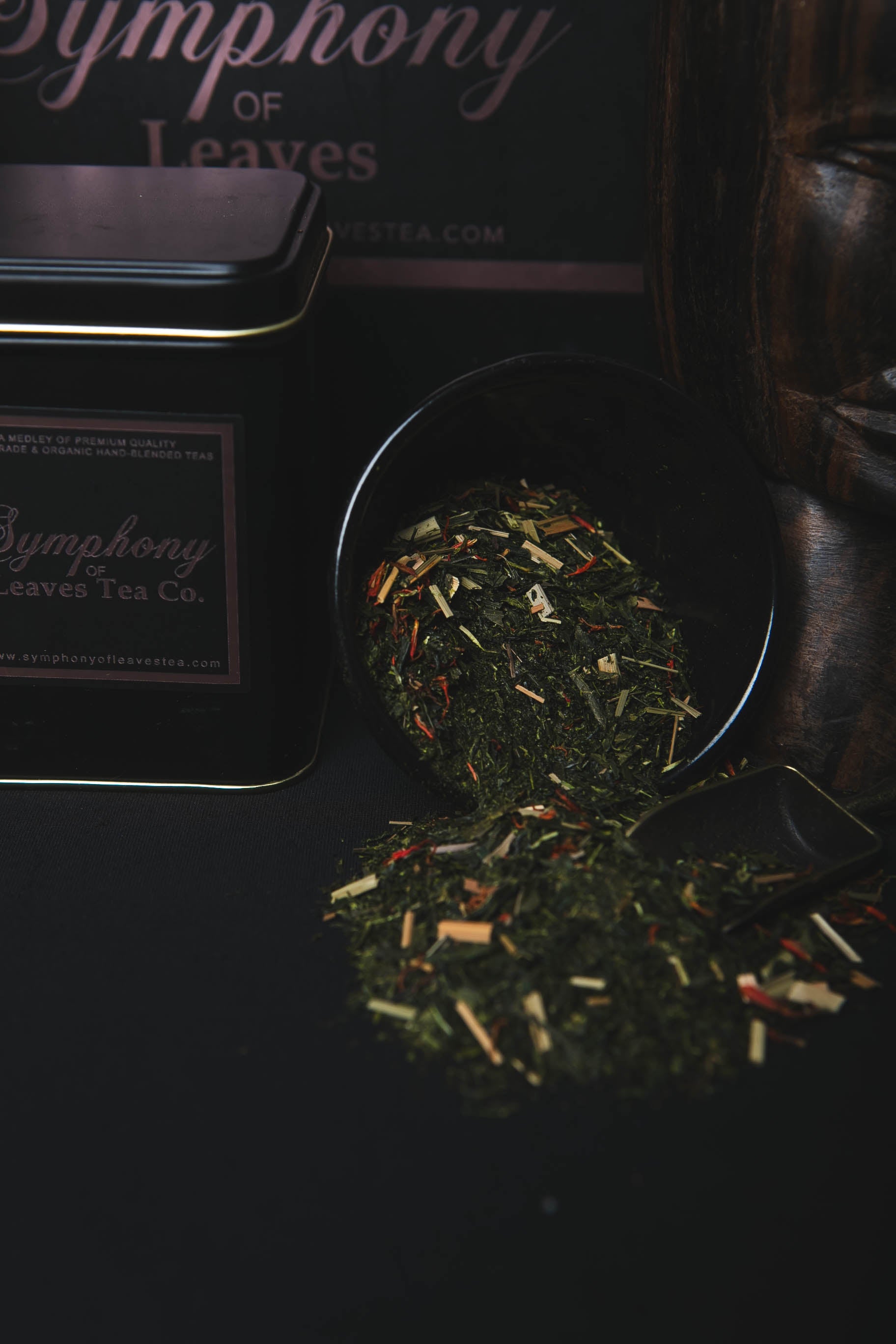 Japanese green leaves blended with safflower and lemongrass in a black scoop with 'Symphony of Leaves Tea Co.' tea canister in the background