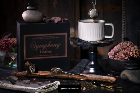 Symphony of Leaves Tea Co.  tea box and decorative elements next to a white tea cup with tea in an infuser