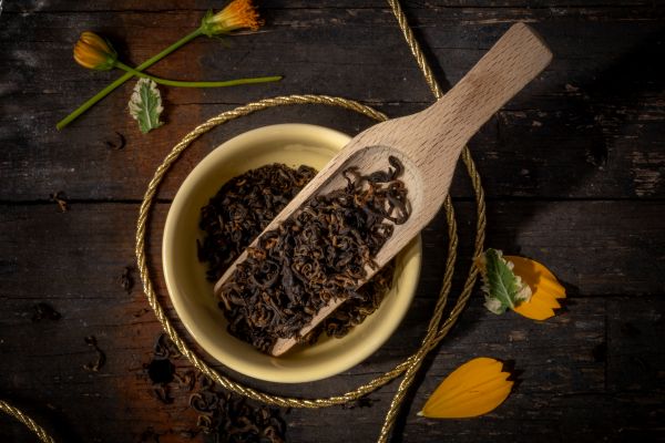 Himalayan black tea leaves in a bowl with a wooden scoop on a dark wooden surface.