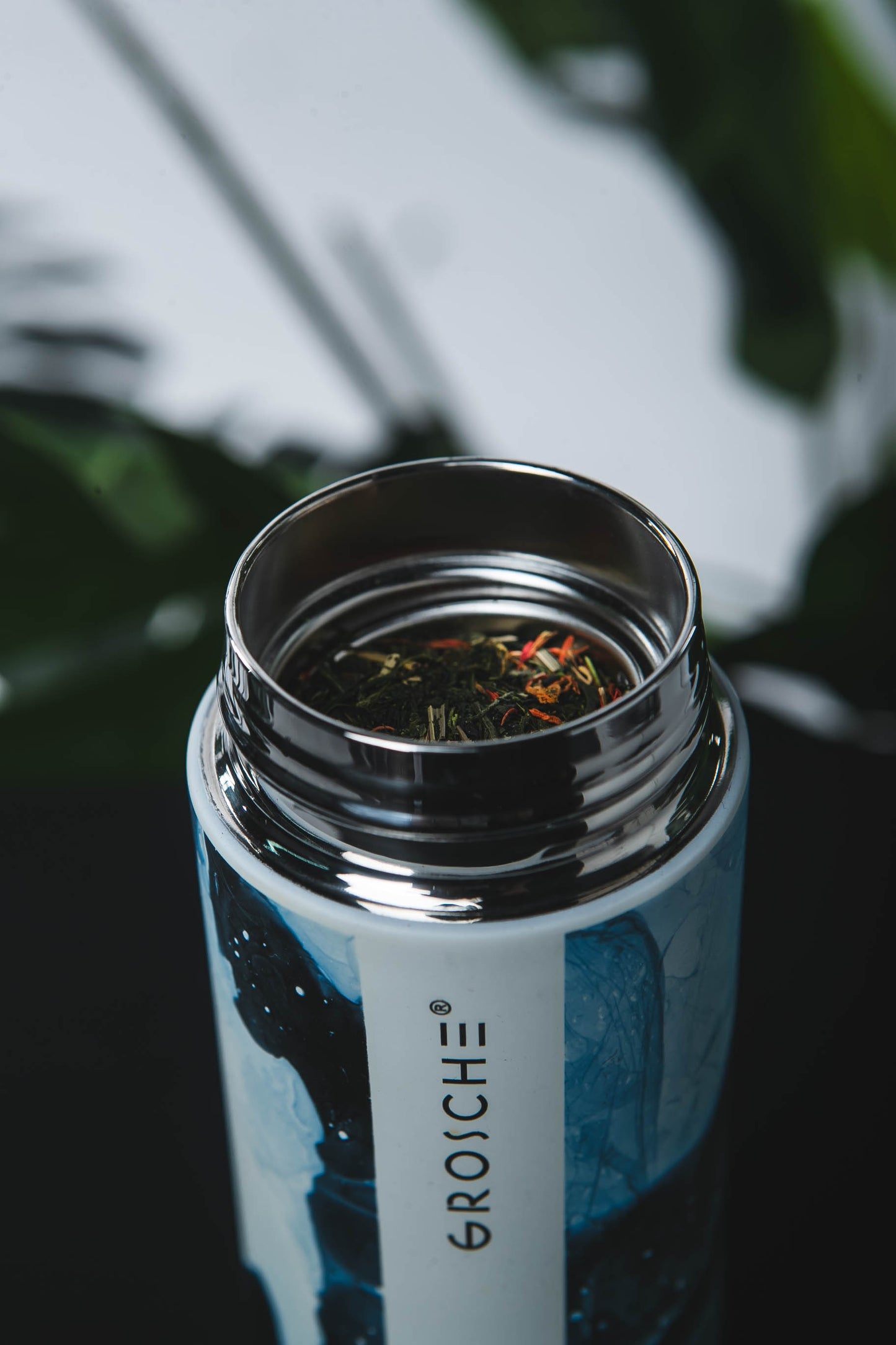 Close-up of a GROSCHE water bottle with tea leaves inside, blurred greenery in the background