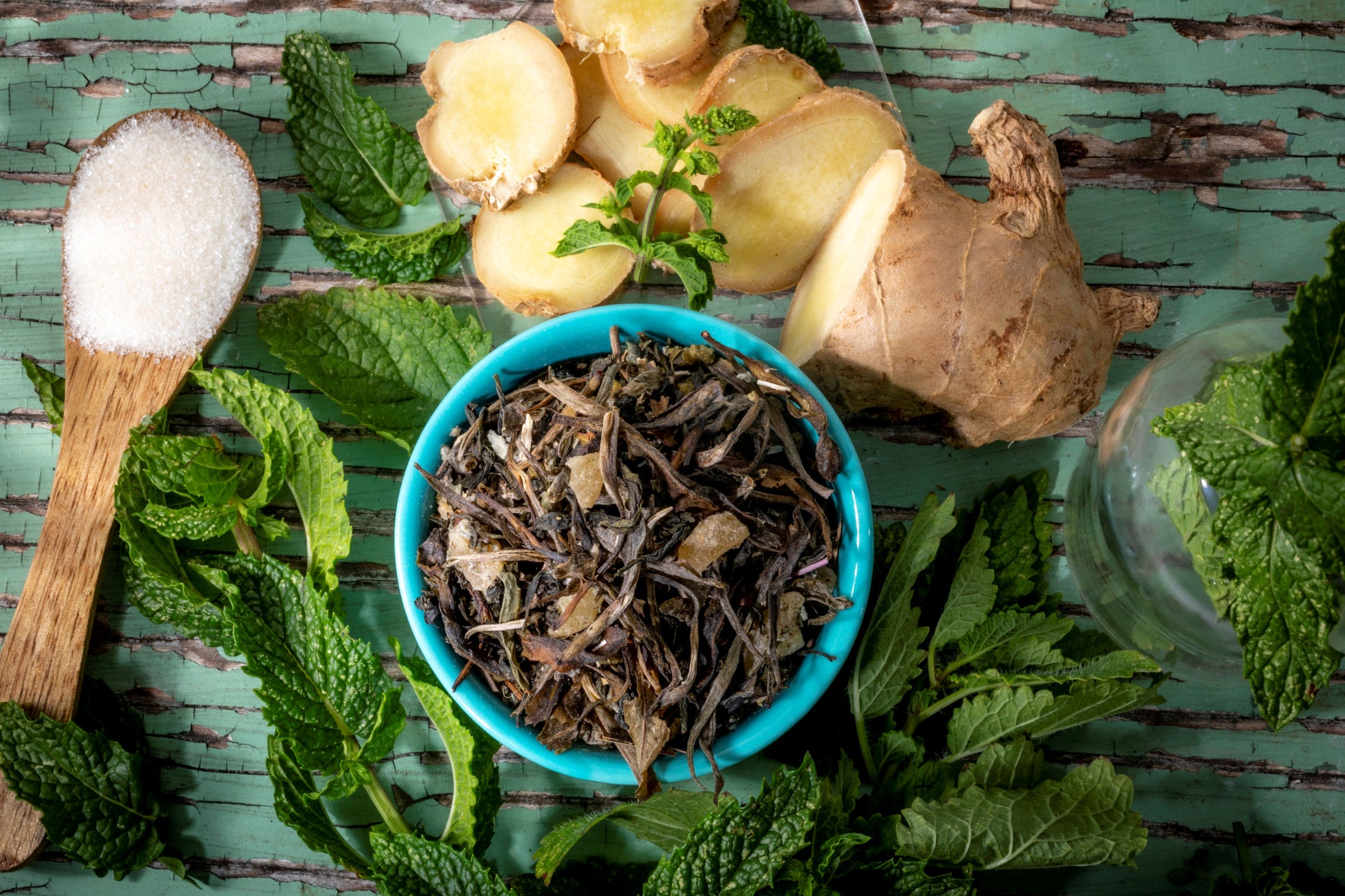 Bhutanese of loose leaf green tea blend ingredients including, fresh mint leaves, ginger, and lemon verbena on a wooden surface.