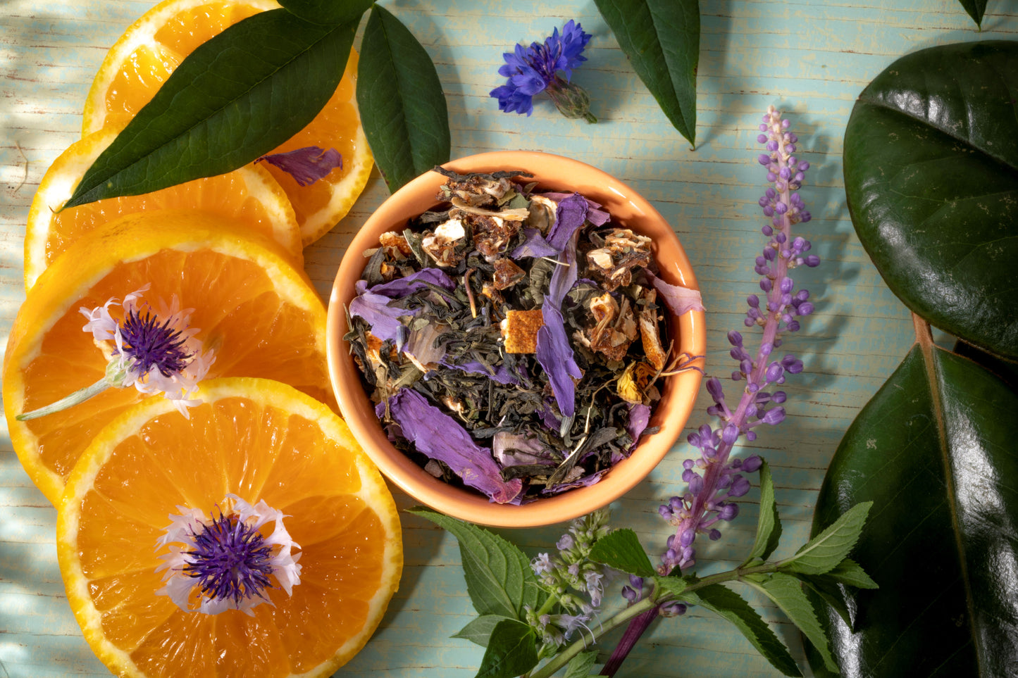 Chinese Green tea leaves and ingredients such as dehydrated tangerines and lemon verbena, butterfly pea arranged on a surface with fresh green leaves and purple flowers.