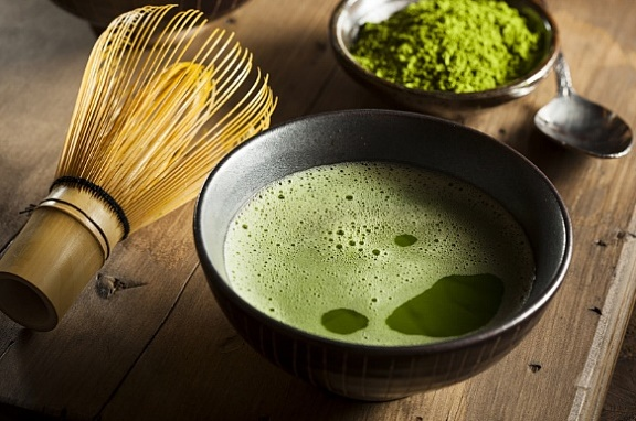 Ceremonial grade Korean malcha green tea in a bowl with a whisk and malcha powder on a wooden surface