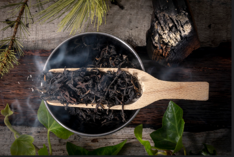 Lapsang Souchong with smoky backgroung in a bowl with a scooper on a piece of wood