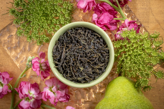 A beautiful display of Chinese loose leaf green tea with pink botanicals and a pear in the background.