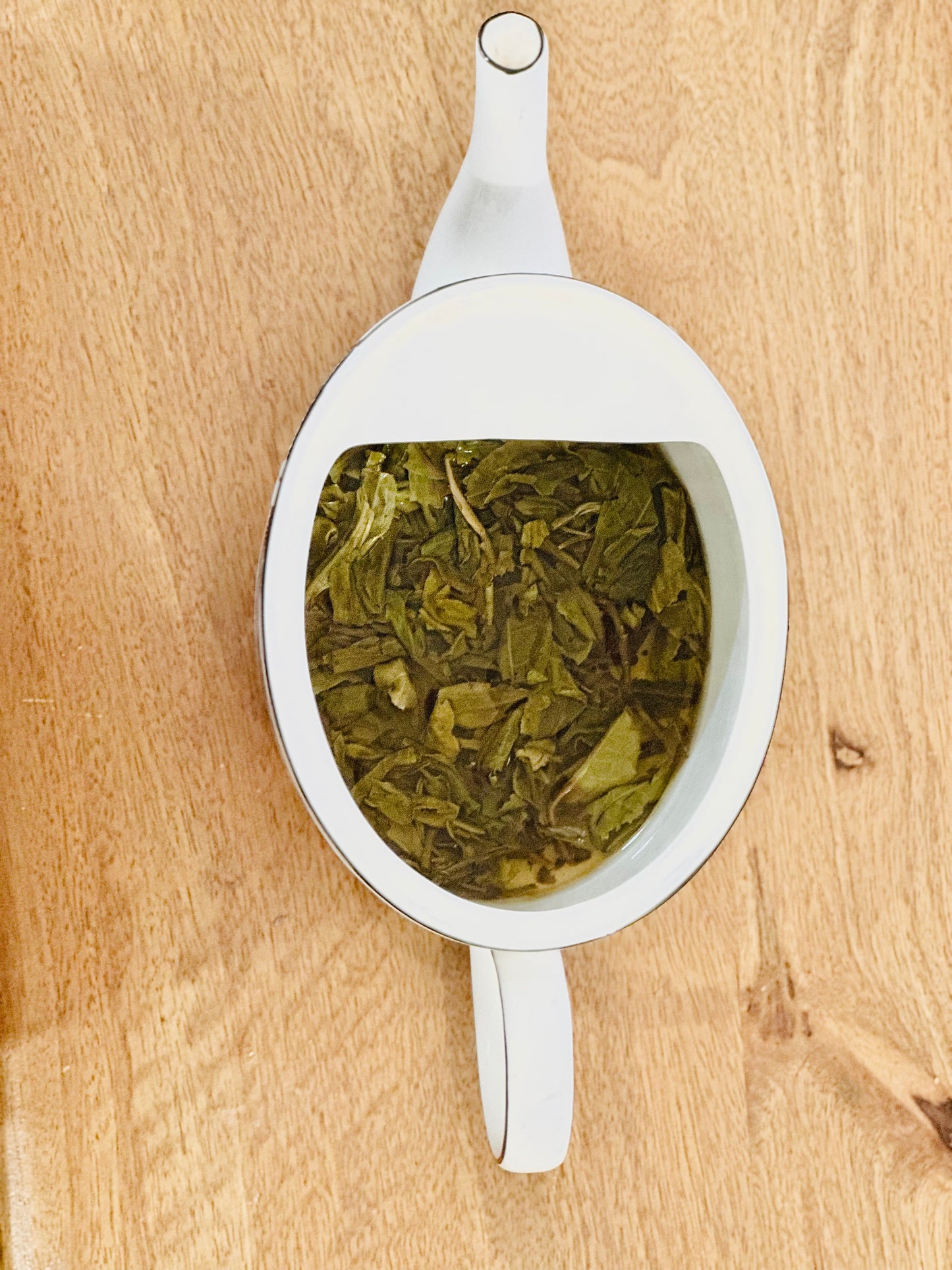 Steeped Vietnamese loose leaf green tea in a white tea pot on a wood board.