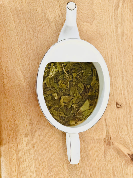 Steeped Vietnamese loose leaf green tea in a white tea pot on a wood board.