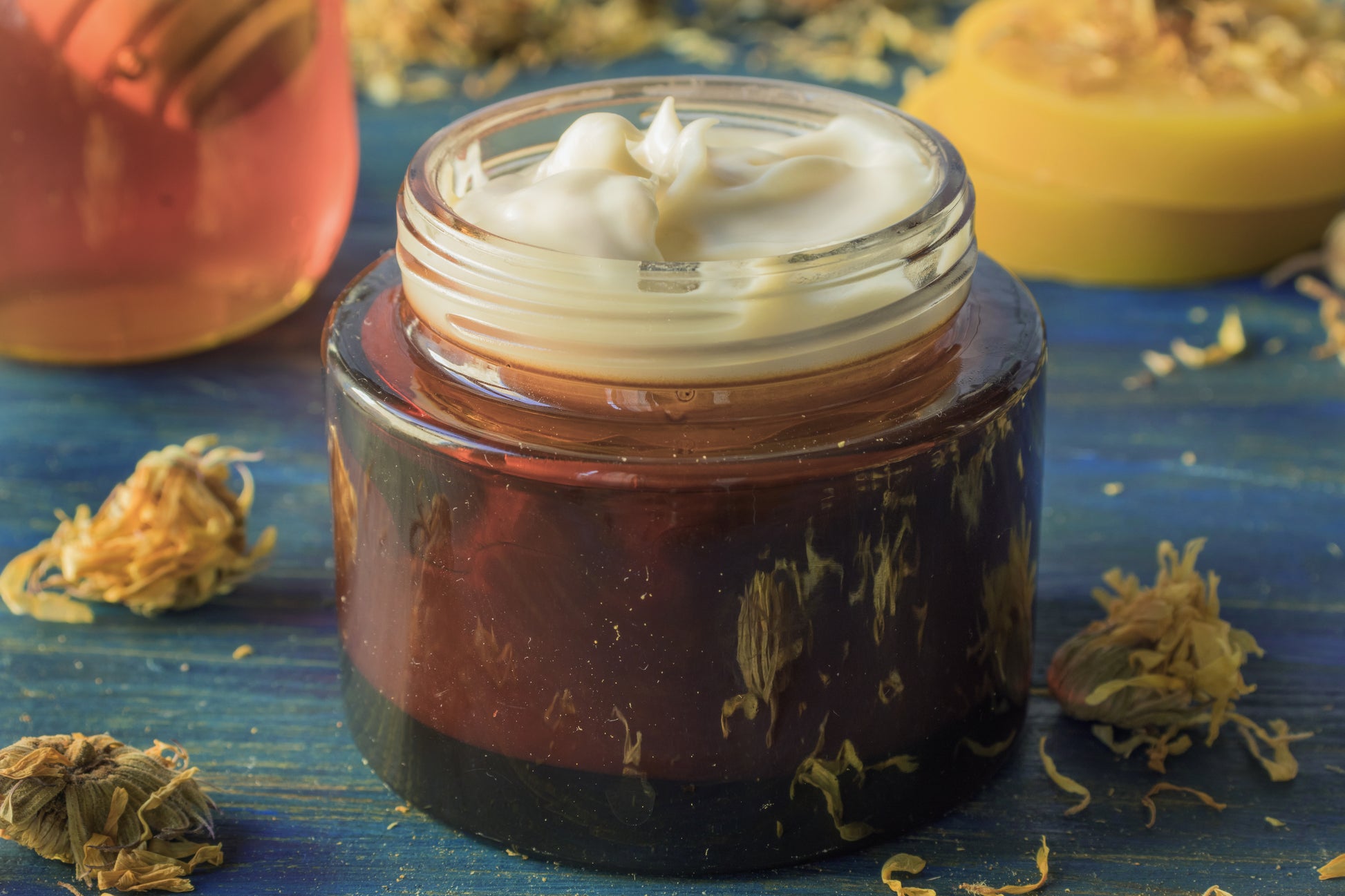 Jar of whipped honey on a blue surface with dried herbs