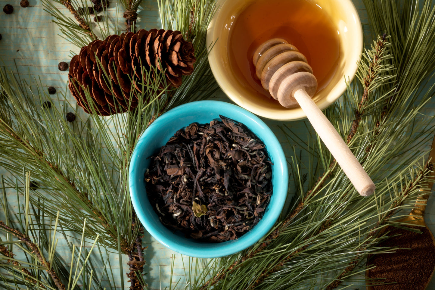 Taiwanese oolong tea leaves in a blue bowl with a honey dipper on pine branches
