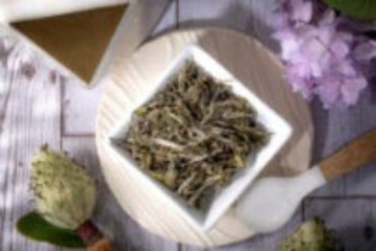 A withered whole loose leaf white tea on a wooden surface, with a pink flower in the background.