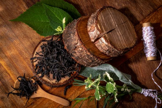 Wooden container with  Dian Hong tea leaves on a wooden surface with green leaves and twine.