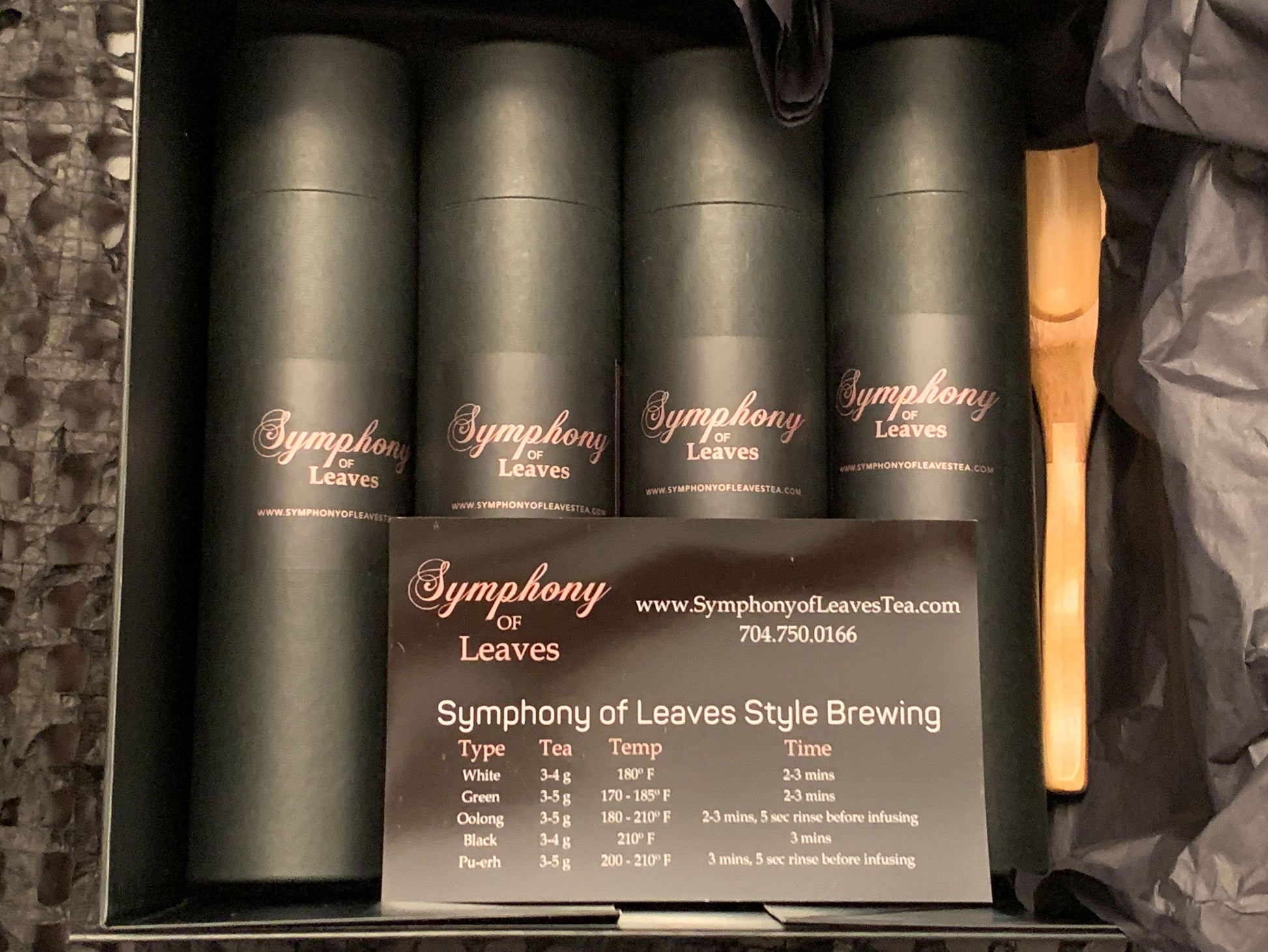 Four artisan tea blends from The Compass Collection displayed in eco-friendly black canisters with rose gold Symphony of Leaves branding