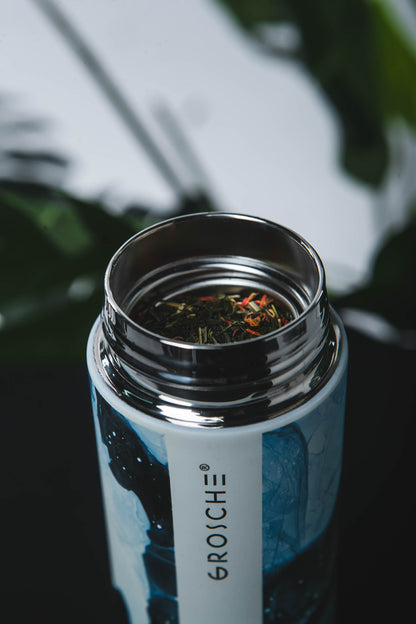 Close-up of a GROSCHE water bottle with tea leaves inside, blurred greenery in the background