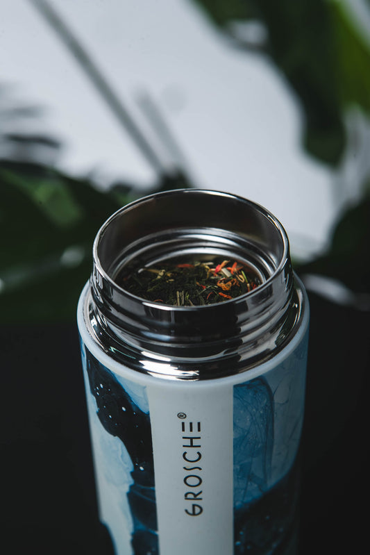 Close-up of a GROSCHE water bottle with tea leaves inside, blurred greenery in the background