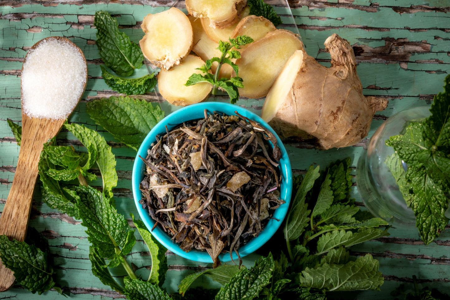 Bhutanese of loose leaf green tea blend ingredients including, fresh mint leaves, ginger, and lemon verbena on a wooden surface.