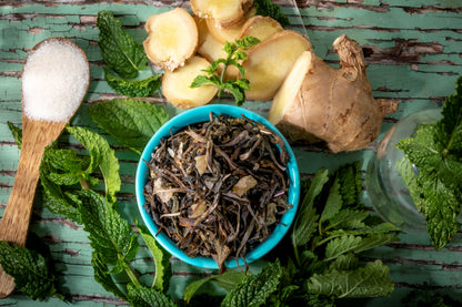 Bhutanese of loose leaf green tea blend ingredients including, fresh mint leaves, ginger, and lemon verbena on a wooden surface.