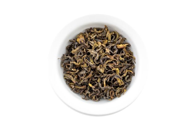 Green dry tea leaves in a white bowl on a white background