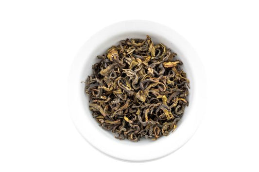 Green dry tea leaves in a white bowl on a white background