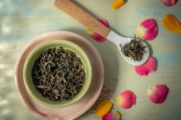 Nepali green Tea leaves in a bowl and on a spoon with colorful petals on a wooden surface