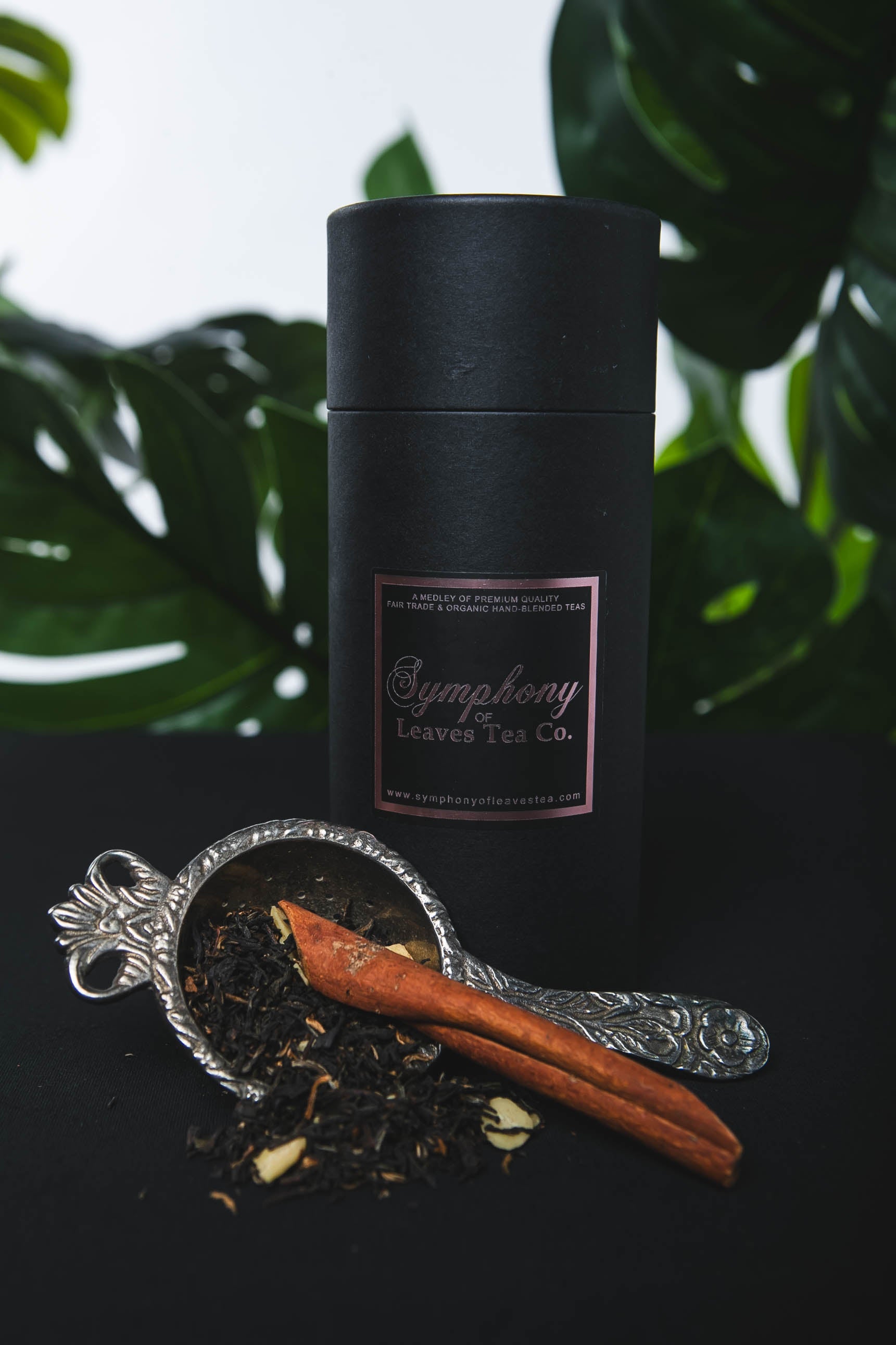 Black cylindrical container with rose gold label on a dark surface with black lapsang souchong tea leaves and cinnamon sticks.