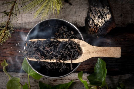 Wooden scoop filled with smoked oolong tea leaves on a rustic wooden surface with greenery.