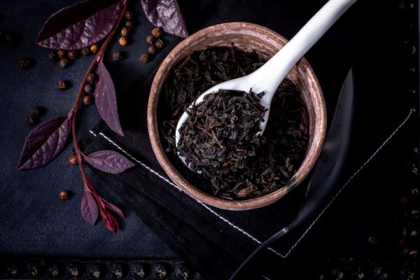 Lapsang Souchong in a wooden bowl with a white spoon on a dark surface