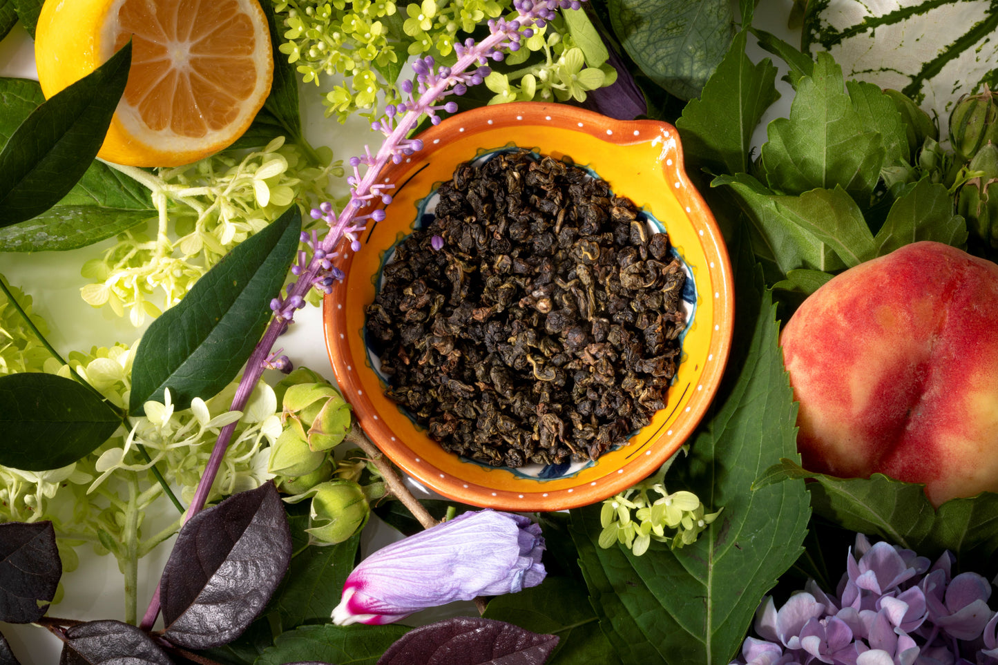 Taiwanese Oolong teas in a small bowl surrounded by peaches, lemons and botanicals and florals.