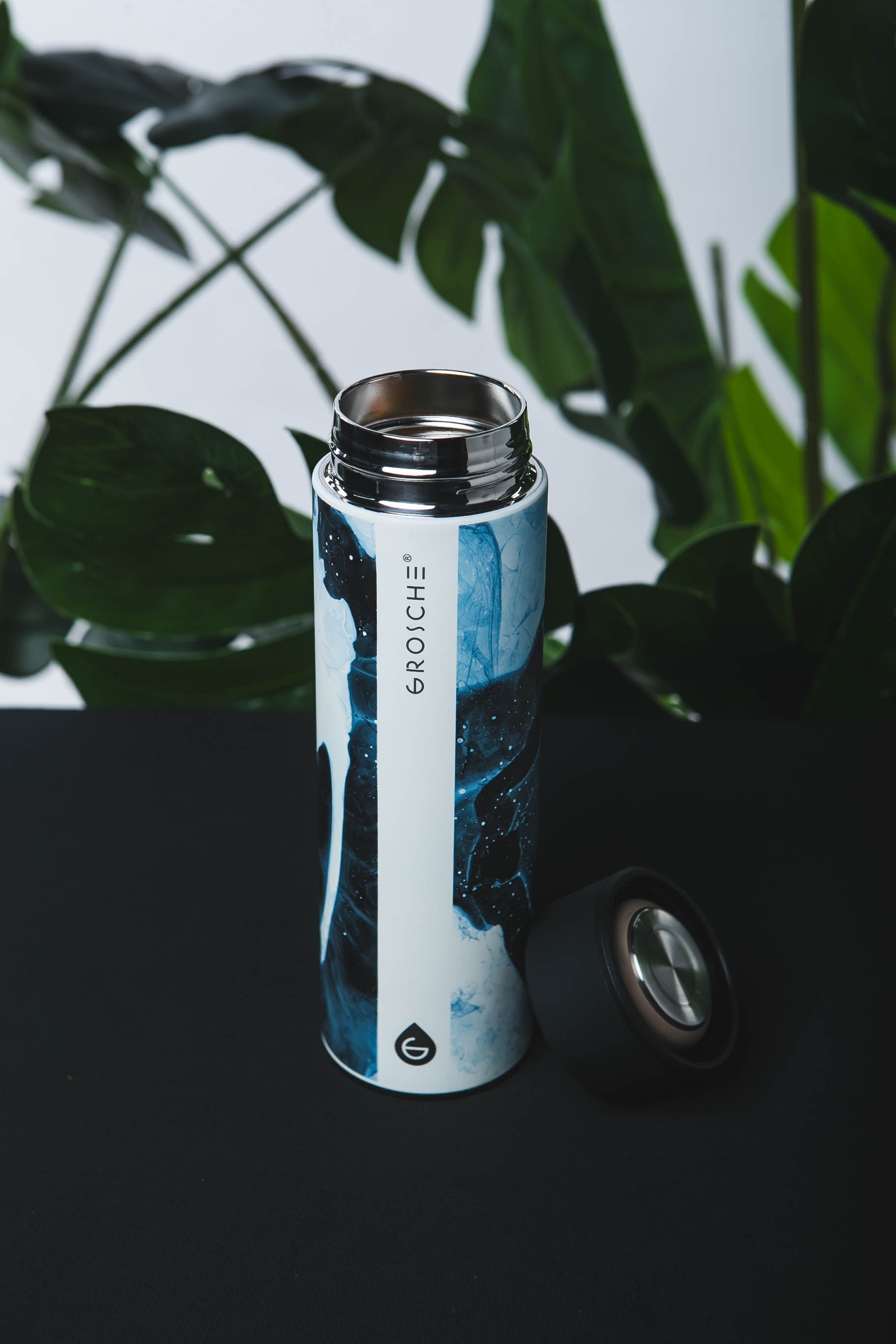 Thermos bottle with a blue design and visible brand logo against a dark background with green leaves.