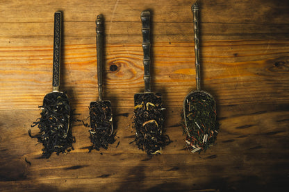 Four metal tea infusers with tea leaves from each of the blends in the Compass Collection on a wooden surface
