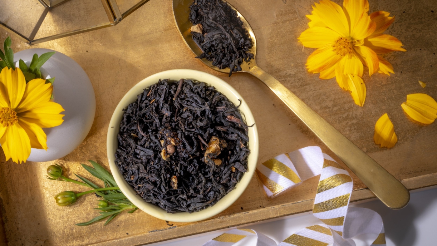 Black tea leaves with golden spoon and flowers