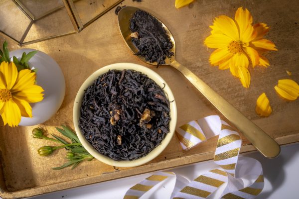 Black tea leaves with golden spoon and flowers