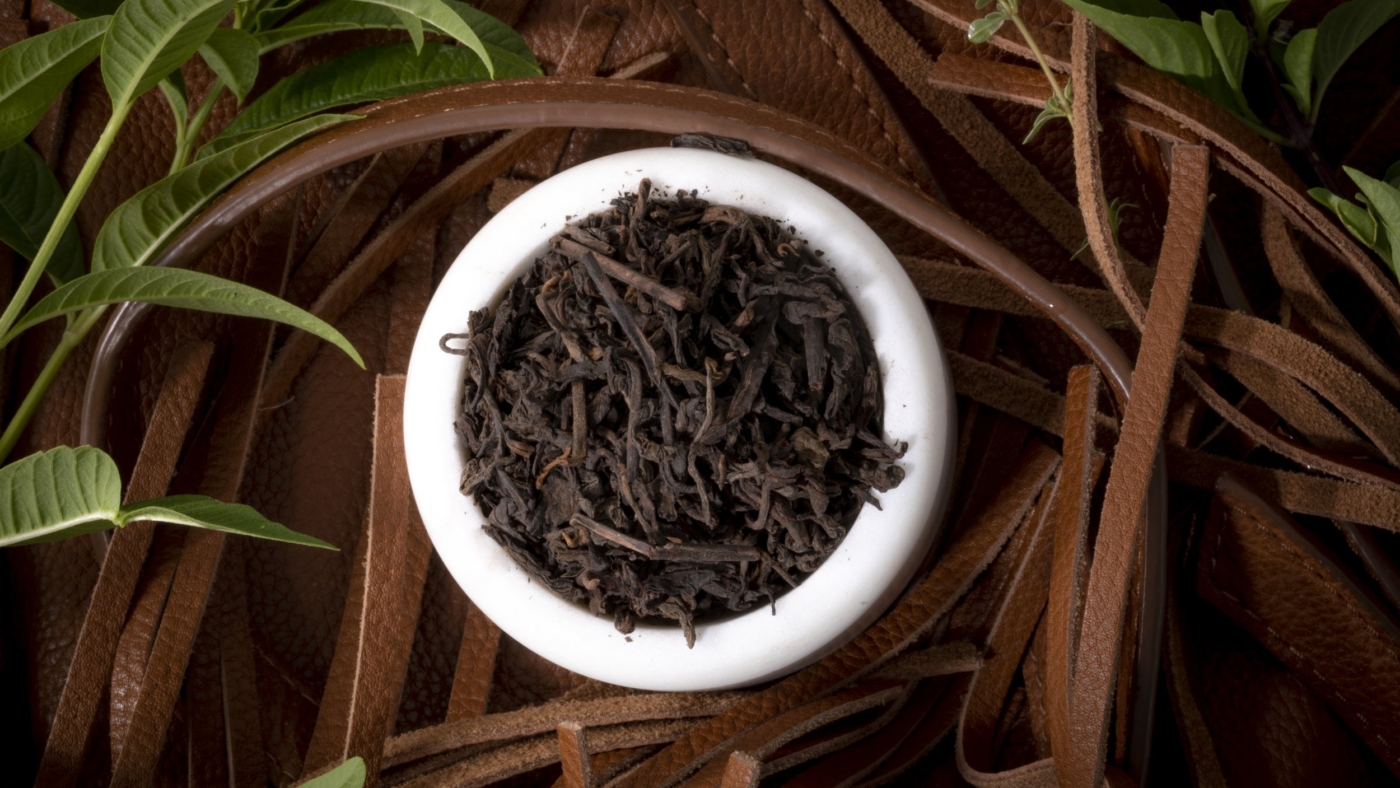 Bowl of black tea with green leaves