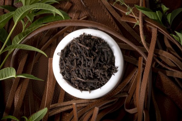 Bowl of black tea with green leaves