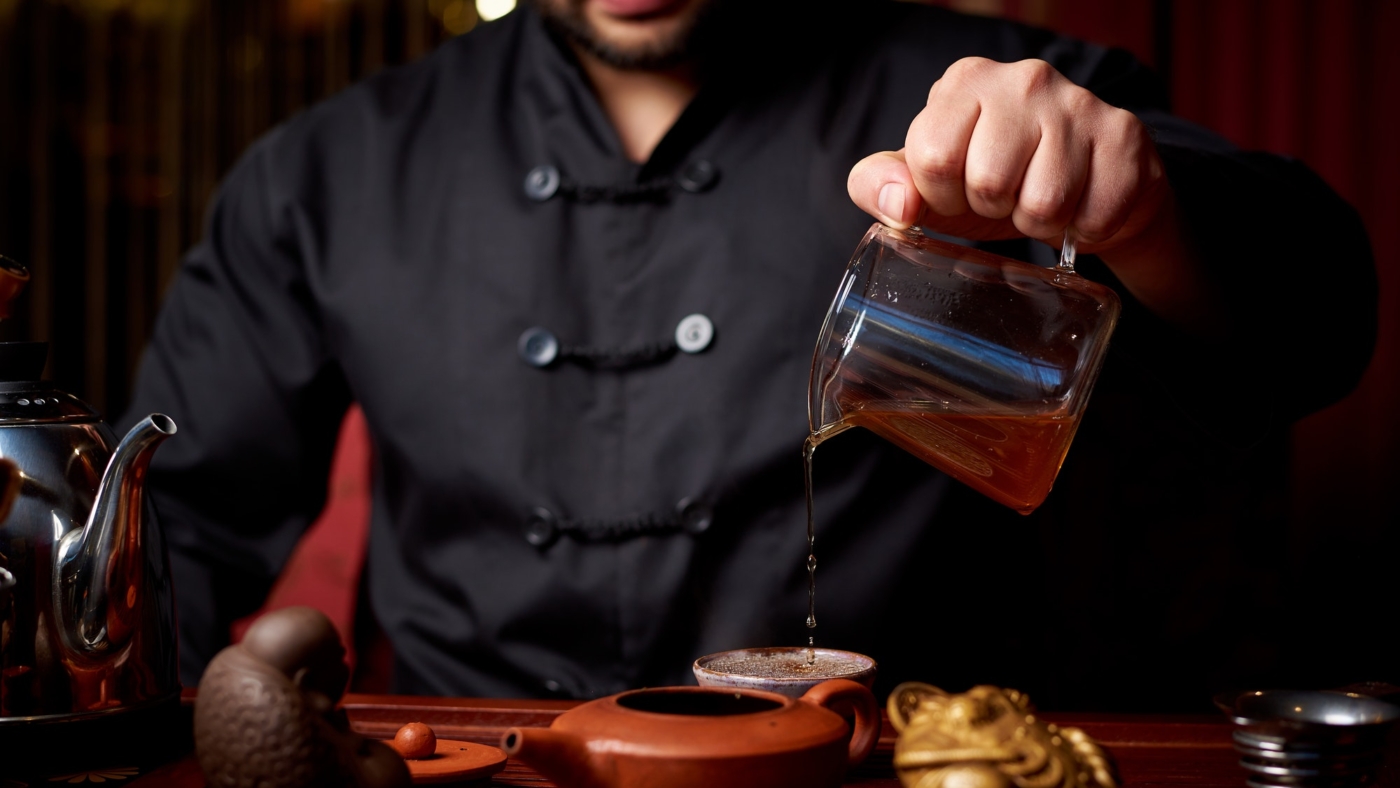 Person pouring tea from glass pot elegantly.