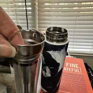 Travel mug with infuser and book nearby.