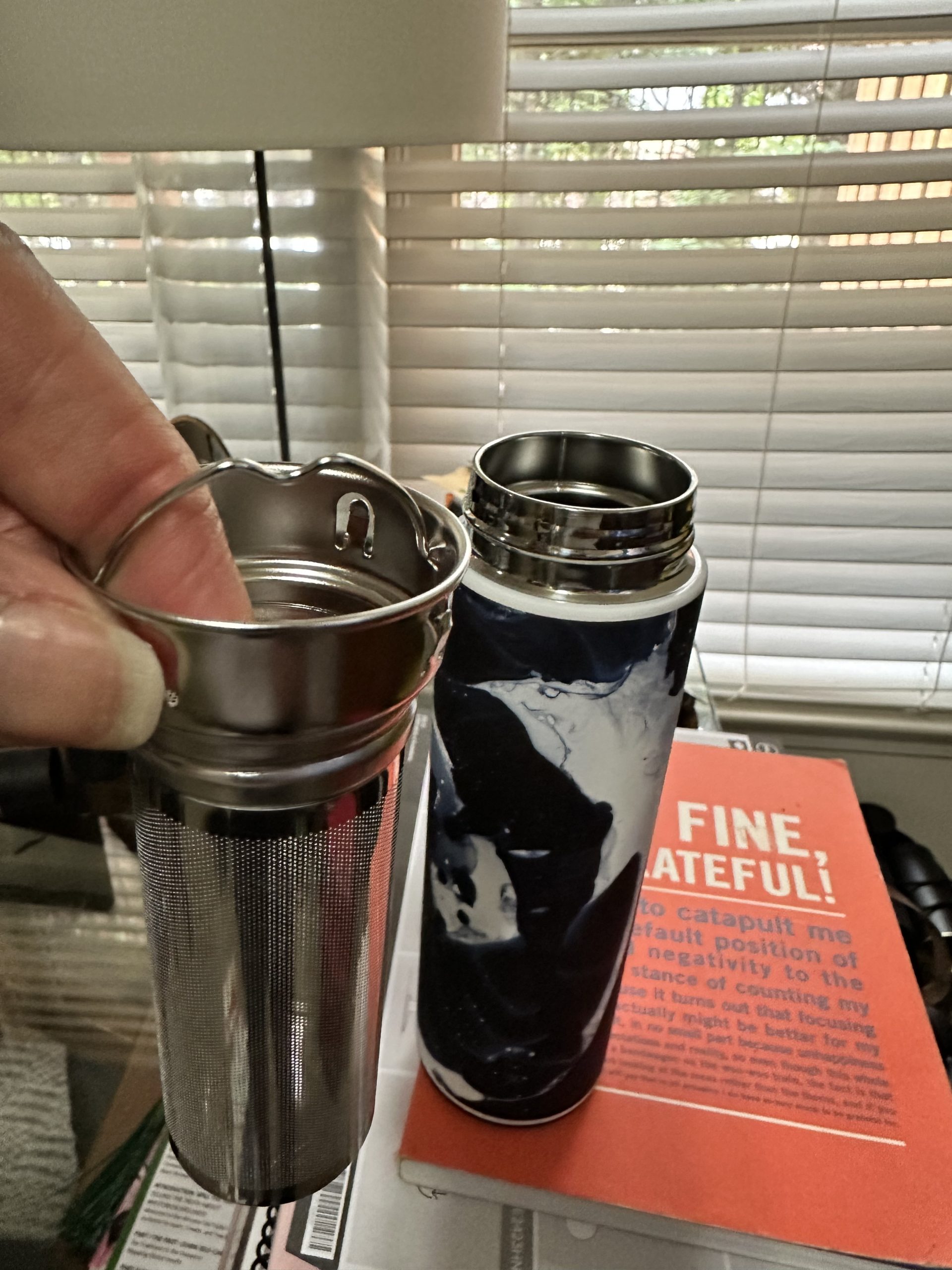 Travel mug with infuser and book nearby.