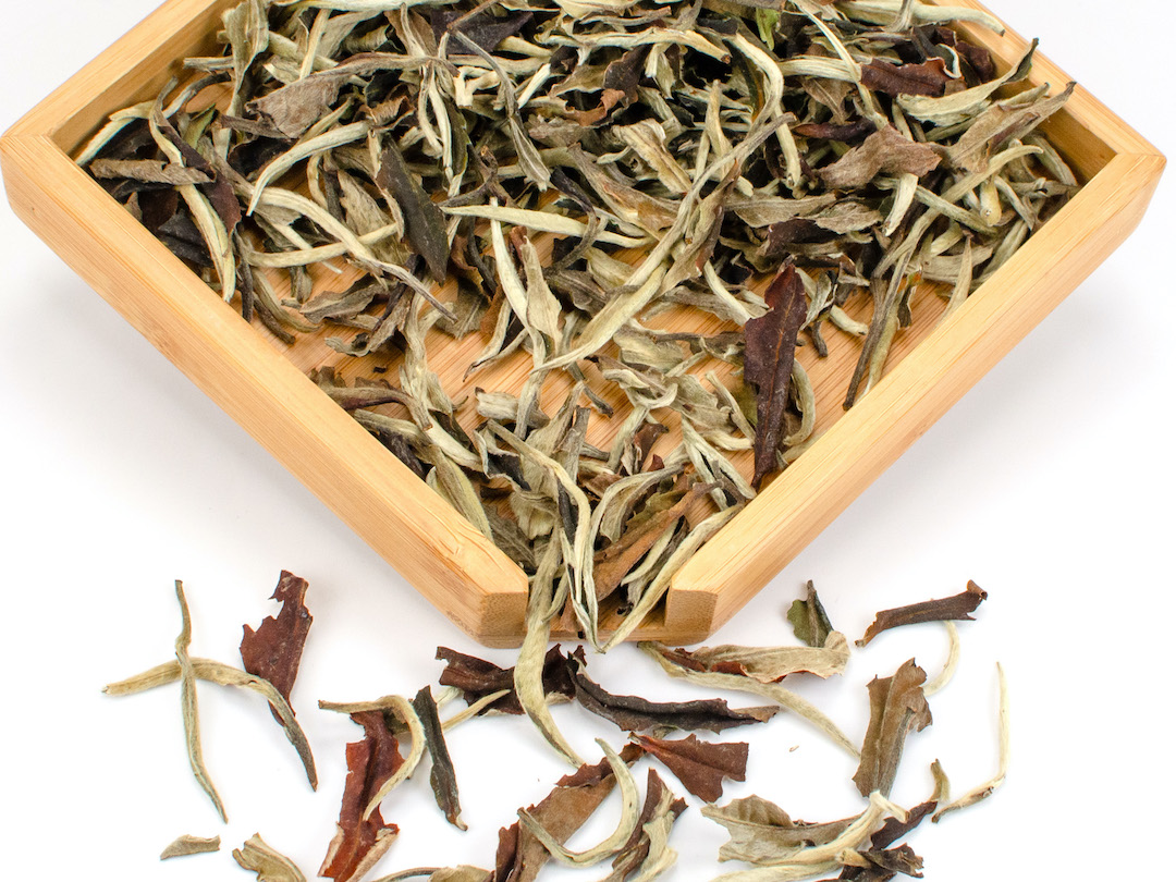 Loose white tea leaves in wooden tray.