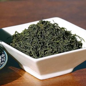 Bowl of dried green tea leaves on table.