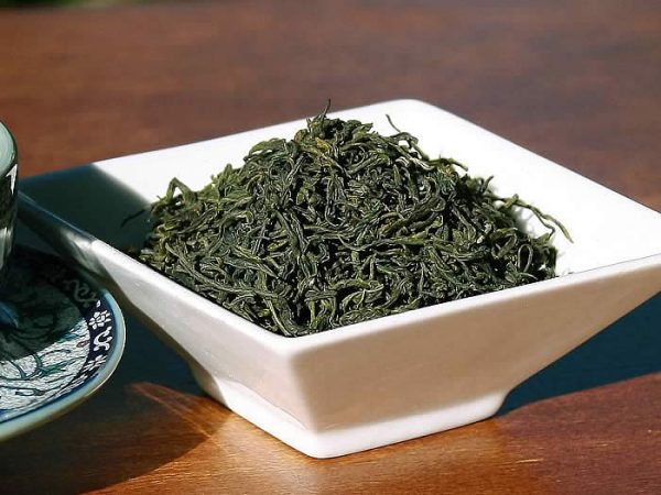 Bowl of dried green tea leaves on table.